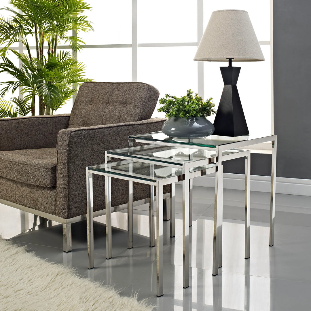 Mesa lateral estilo nido de acero inoxidable y vidrio templado Griselda en una sala.