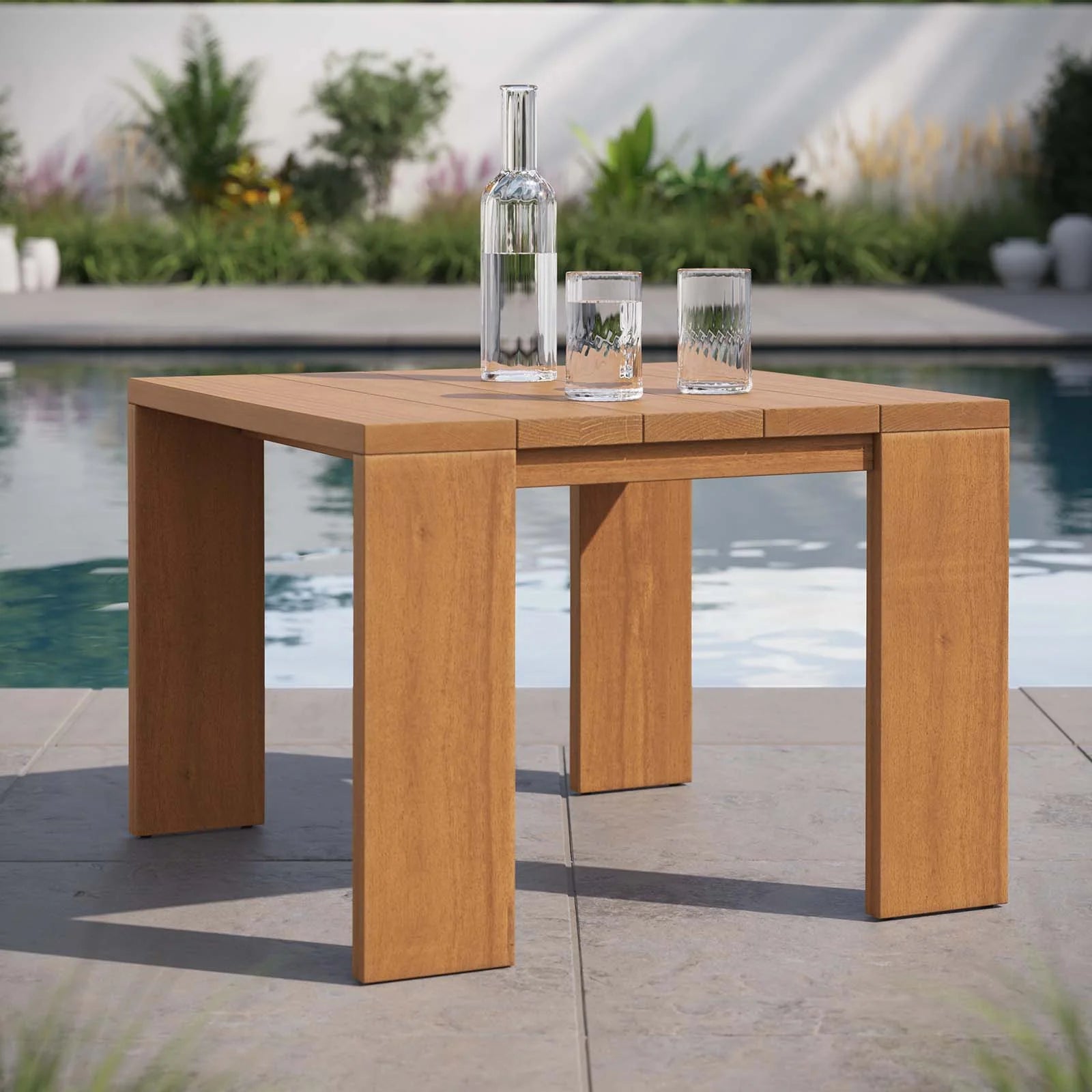 Mesa lateral para exteriores de madera de acacia Neuba al lado de una alberca.