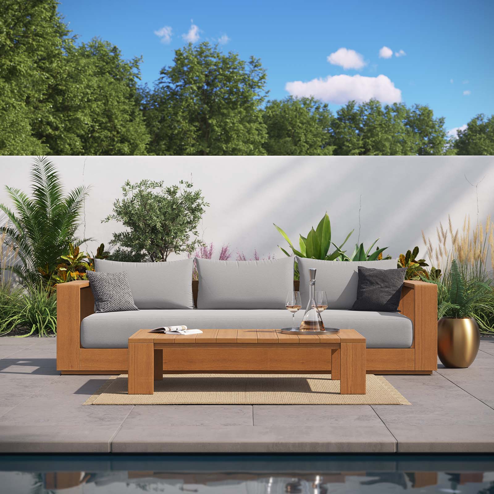 Sillón y mesa de centro para exteriores de madera de acacia Nueba frente a una alberca.