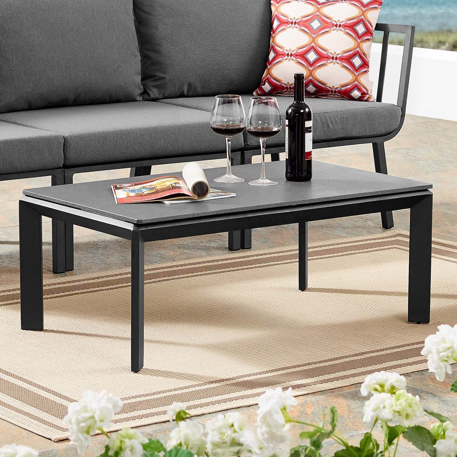 Mesa de centro exterior de aluminio y concreto Loana ALOA-01 color de la base negra y superficie de concreto negro en un patio exterior, encima dos copas de vino y dos revistas.